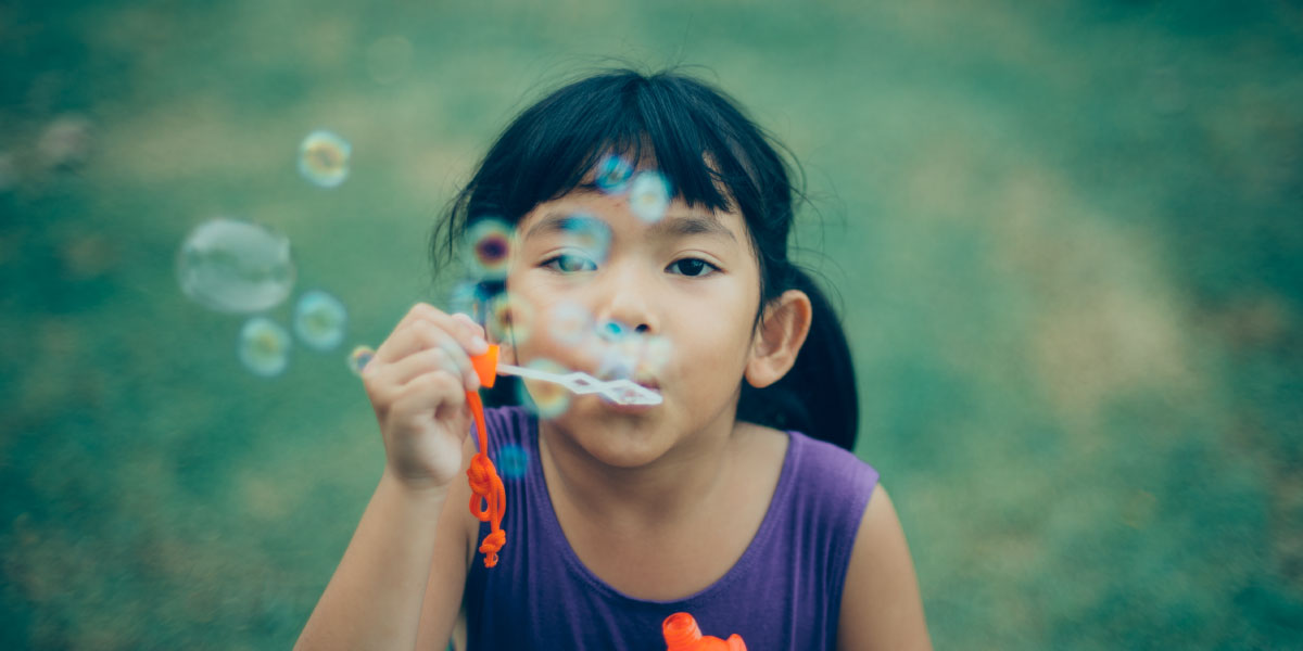 Young girl makes soap bubbles outdoors.